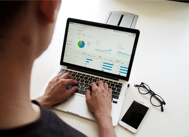 Image shows over the shoulder of a person using a laptop with data visualised in charts on the screen